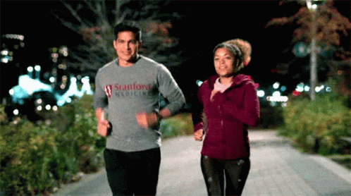A Man In A Stanford Medicine Shirt Is Jogging Next To A Woman GIF