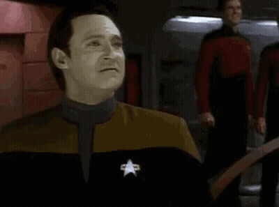 A Man In A Star Trek Uniform Is Making A Funny Face While Standing In Front Of A Group Of People . GIF