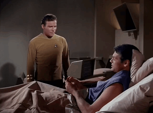 A Man In A Star Trek Uniform Is Standing Next To Another Man In A Hospital Bed GIF