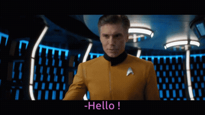 A Man In A Star Trek Uniform Says Hello In A Dark Room GIF