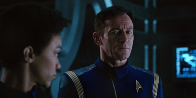 A Man In A Star Trek Uniform Talks To Another Man In A Dark Room GIF