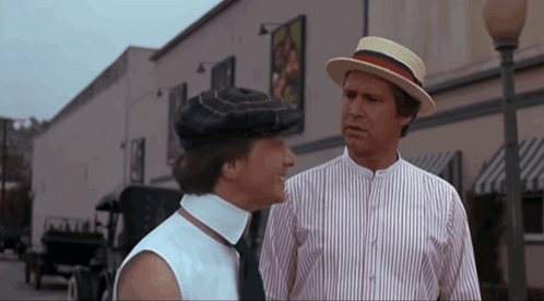 A Man In A Straw Hat Talks To A Woman In A Striped Shirt GIF