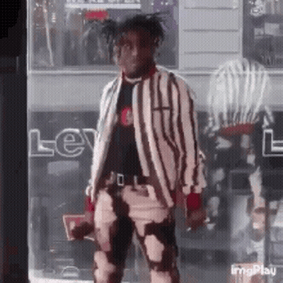 A Man In A Striped Jacket And Pants Is Standing In Front Of A Store . GIF