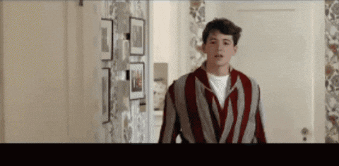 A Man In A Striped Jacket Is Standing In A Hallway . GIF