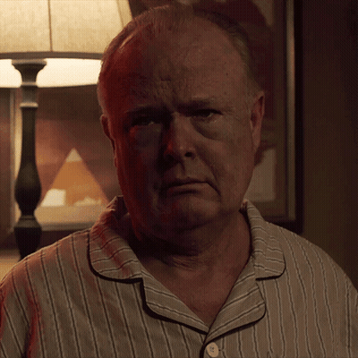 A Man In A Striped Pajama Shirt Looks At The Camera With A Lamp In The Background GIF