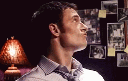 A Man In A Striped Shirt And Tie Is Looking Up In A Room With Pictures On The Wall . GIF