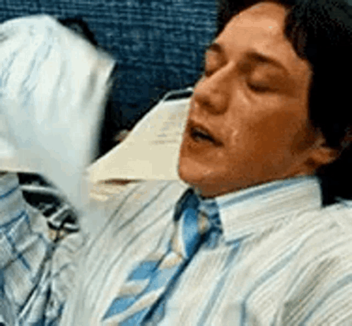 A Man In A Striped Shirt And Tie Is Sleeping On A Chair . GIF