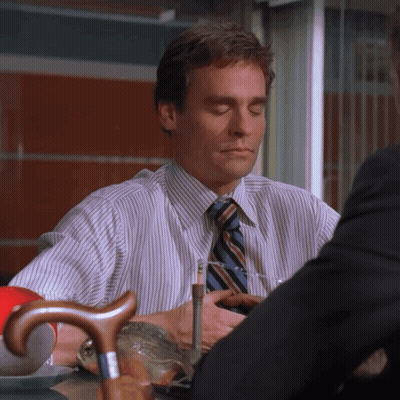 A Man In A Striped Shirt And Tie Sits At A Table GIF