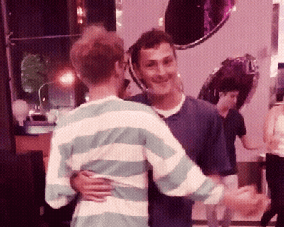 A Man In A Striped Shirt Hugs Another Man In A Blue Shirt GIF