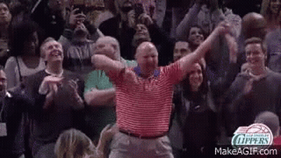 A Man In A Striped Shirt Is Dancing In Front Of A Crowd Of People . GIF