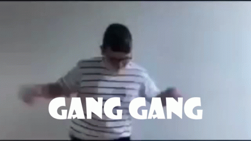 A Man In A Striped Shirt Is Dancing In Front Of A Wall With Gang Gang Written On It GIF