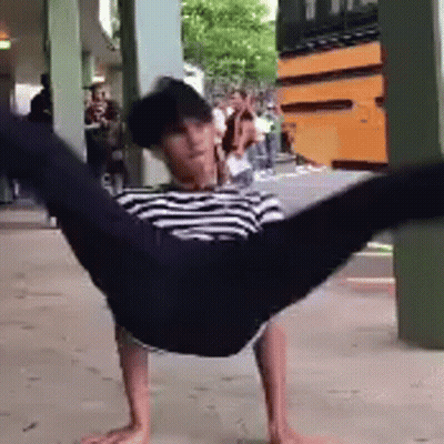 A Man In A Striped Shirt Is Doing A Handstand In Front Of A School Bus . GIF