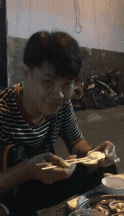 A Man In A Striped Shirt Is Eating Food With Chopsticks And Smiling GIF