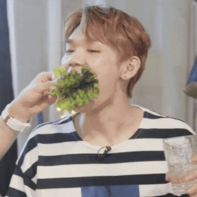 A Man In A Striped Shirt Is Eating Lettuce While Holding A Glass . GIF