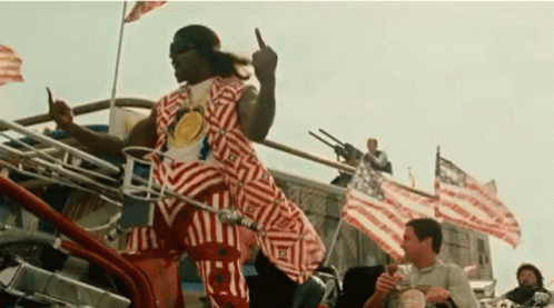A Man In A Striped Shirt Is Giving The Middle Finger While Riding A Motorcycle . GIF