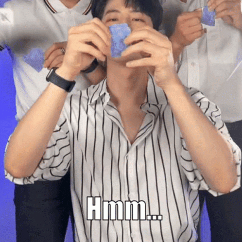 A Man In A Striped Shirt Is Holding A Blue Object In His Hands And Says Hmm GIF