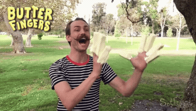 A Man In A Striped Shirt Is Holding A Piece Of Butter In Front Of A Sign That Says Butter Fingers GIF