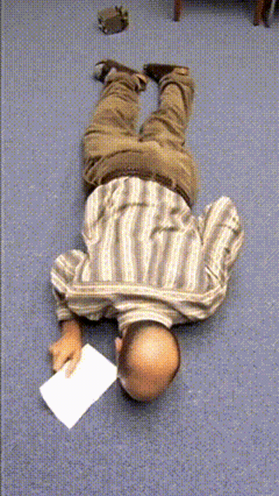 A Man In A Striped Shirt Is Laying On His Back On The Floor Holding A Piece Of Paper GIF