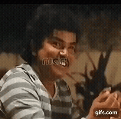A Man In A Striped Shirt Is Making A Funny Face While Holding A Cell Phone . GIF
