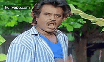 A Man In A Striped Shirt Is Making A Funny Face While Standing In Front Of A Tree . GIF