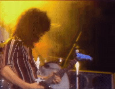 A Man In A Striped Shirt Is Playing A Guitar On Stage GIF