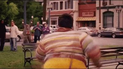 A Man In A Striped Shirt Is Running In A Park In Front Of A Store That Says Sri Lankan GIF