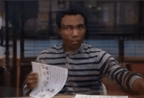 A Man In A Striped Shirt Is Sitting At A Desk With A Piece Of Paper In His Hand GIF