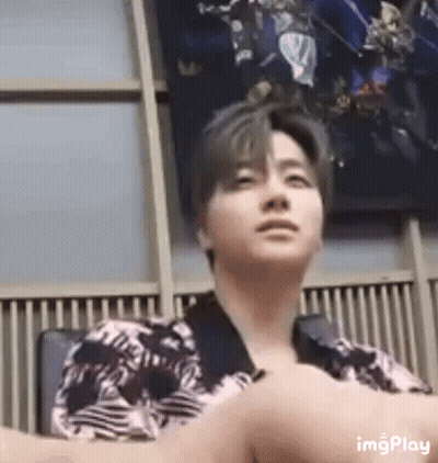 A Man In A Striped Shirt Is Sitting In A Chair With His Arms Crossed . GIF