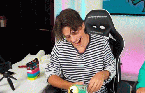 A Man In A Striped Shirt Is Sitting In A Dxracer Chair Laughing GIF