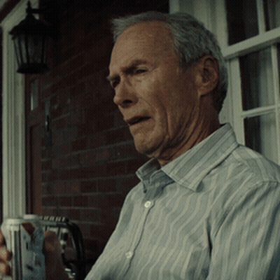 A Man In A Striped Shirt Is Sitting On A Porch Holding A Cup GIF