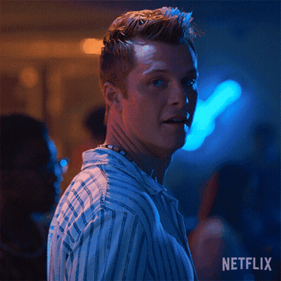 A Man In A Striped Shirt Is Smiling In A Dark Room With Blue Lights . GIF