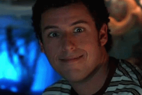 A Man In A Striped Shirt Is Smiling In Front Of A Computer Screen . GIF