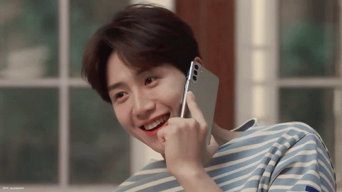 A Man In A Striped Shirt Is Smiling While Holding A Phone GIF
