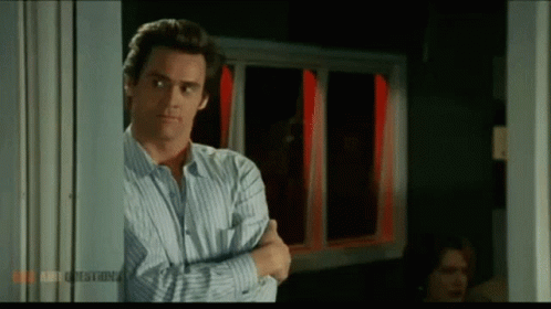 A Man In A Striped Shirt Is Standing In A Doorway With His Arms Crossed In Front Of A Window . GIF