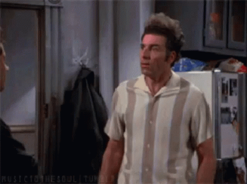 A Man In A Striped Shirt Is Standing In A Kitchen Next To A Refrigerator . GIF
