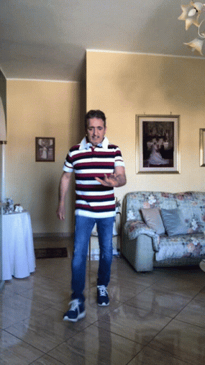 A Man In A Striped Shirt Is Standing In A Living Room In Front Of A Couch GIF