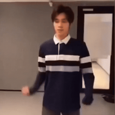A Man In A Striped Shirt Is Standing In A Room . GIF