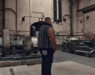 A Man In A Striped Shirt Is Standing In A Room With A Sign On The Wall That Says ' Ts ' GIF