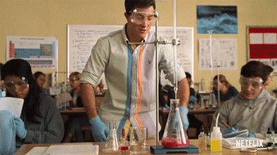 A Man In A Striped Shirt Is Standing In Front Of A Beaker With Red Liquid In It GIF