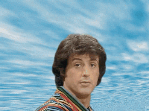 A Man In A Striped Shirt Is Standing In Front Of A Joke Sign GIF