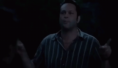 A Man In A Striped Shirt Is Standing In The Dark And Talking . GIF