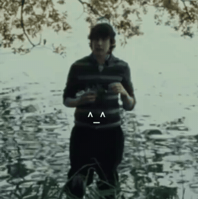 A Man In A Striped Shirt Is Standing In The Water With A Smiley Face On His Belt GIF