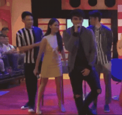 A Man In A Striped Shirt Is Standing Next To A Woman In A Yellow Dress On A Red Carpet GIF