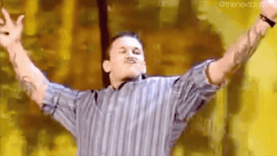 A Man In A Striped Shirt Is Standing With His Arms Outstretched On A Stage . GIF