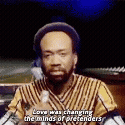 A Man In A Striped Shirt Is Talking Into A Microphone And Says `` Love Was Changing The Minds Of Pretenders '' . GIF