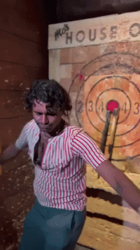 A Man In A Striped Shirt Is Throwing An Axe At A Target That Says Moss House GIF