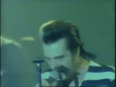 A Man In A Striped Shirt Singing Into A Microphone . GIF