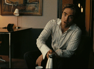 A Man In A Striped Shirt Sits In Front Of A Table GIF