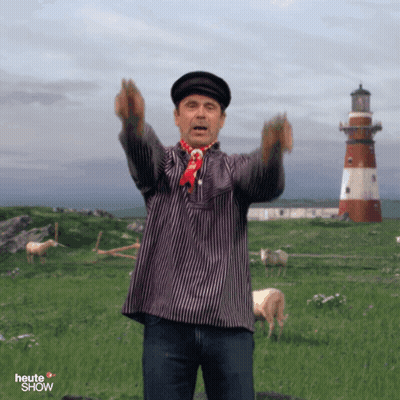 A Man In A Striped Shirt Stands In A Field With A Lighthouse In The Background And The Word Heute Show On The Bottom GIF