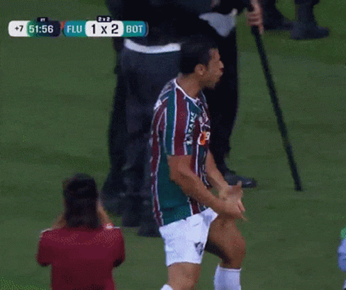 A Man In A Striped Shirt Stands On A Soccer Field With A Score Of 1 X 2 GIF